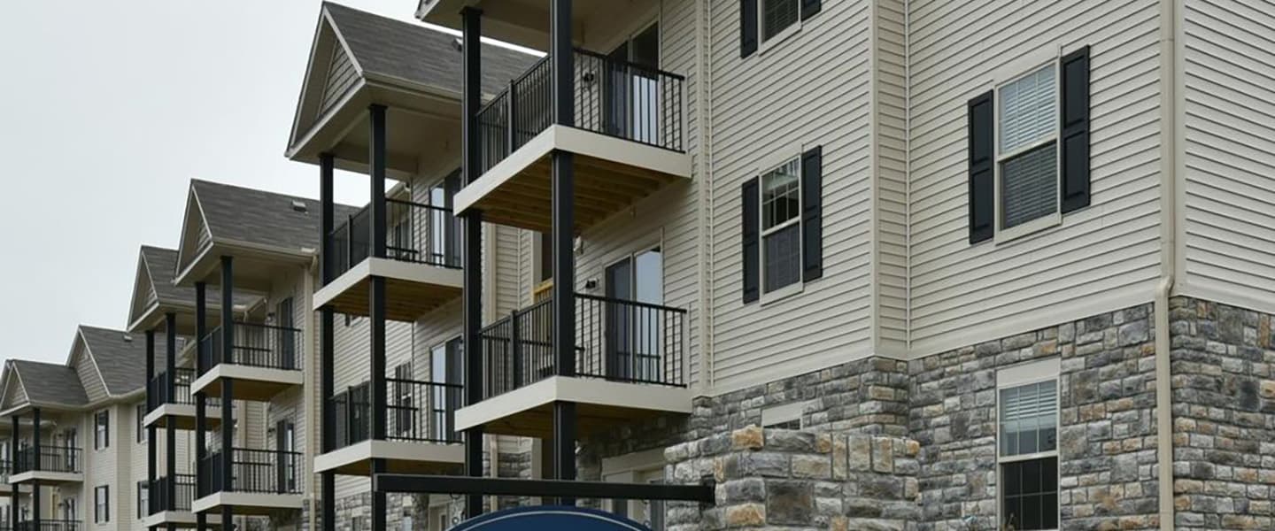 A front-view of an apartment building with inviting landscaping details including trees and bushes.