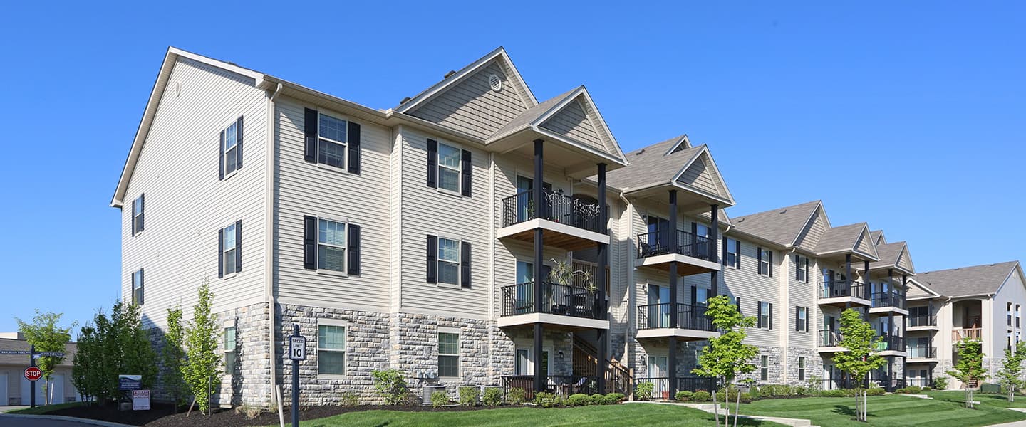 A front-view of an apartment building with inviting landscaping details including trees and bushes.