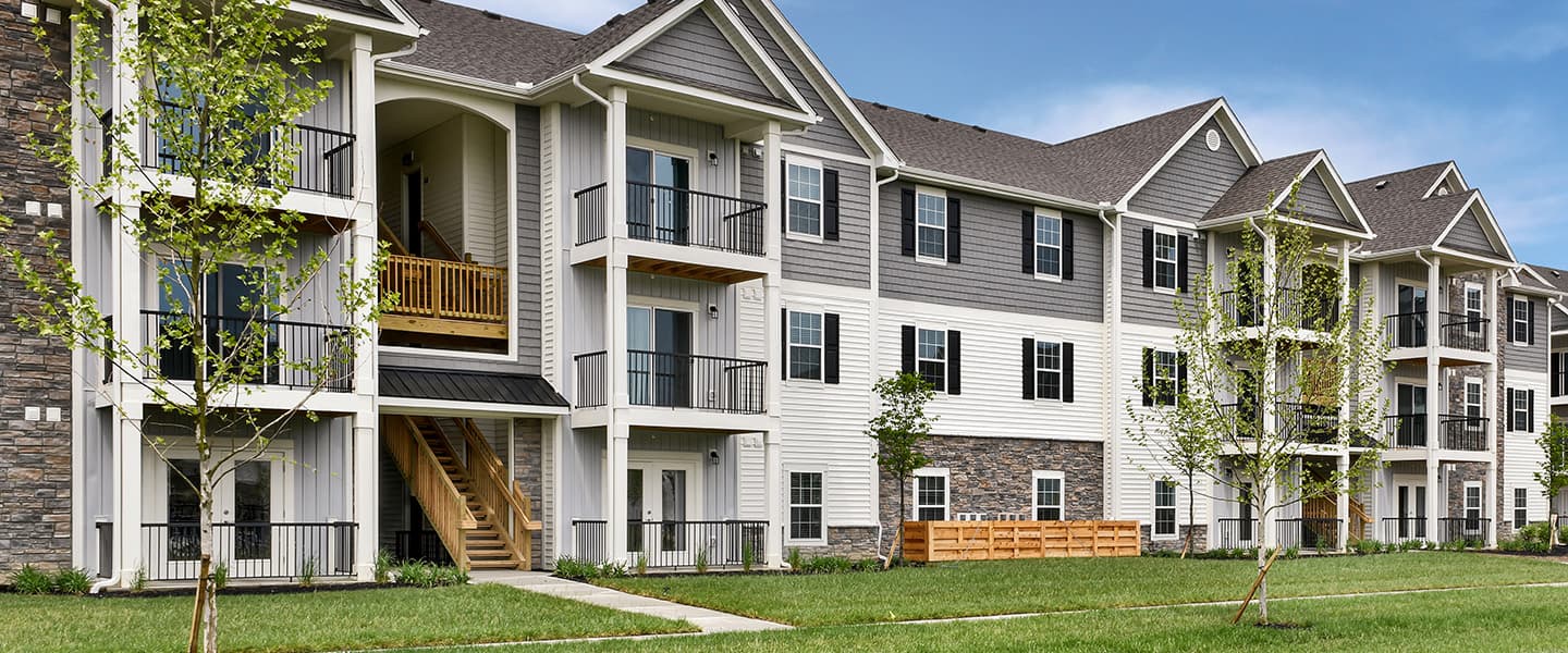 A front-view of an apartment building with inviting landscaping details including trees and bushes.
