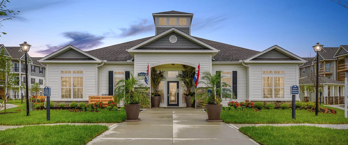 A front-view of an apartment building with inviting landscaping details including trees and bushes.