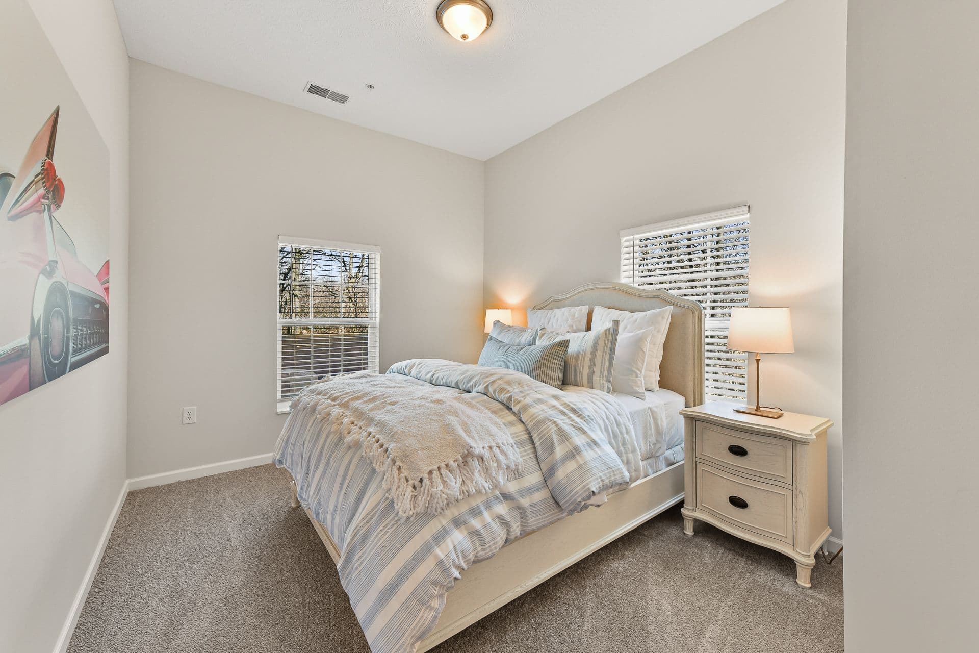 A bedroom with a bed, two nightstands and two windows