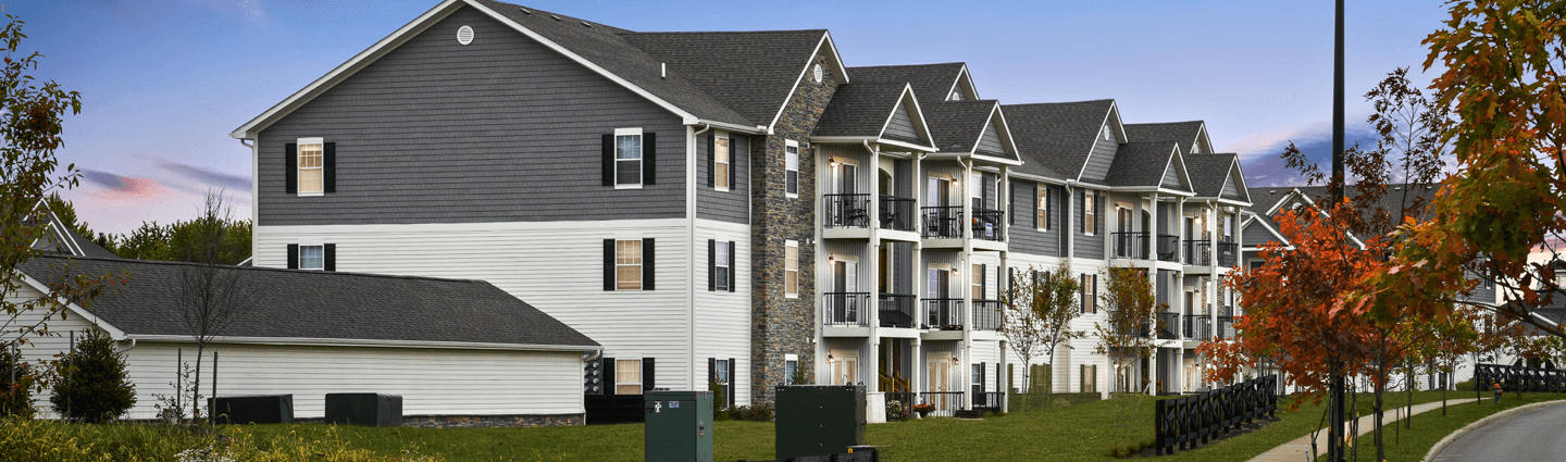 A front-view of an apartment building with inviting landscaping details including trees and bushes.