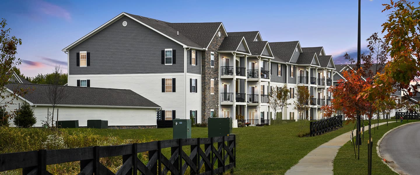 A front-view of an apartment building with inviting landscaping details including trees and bushes.