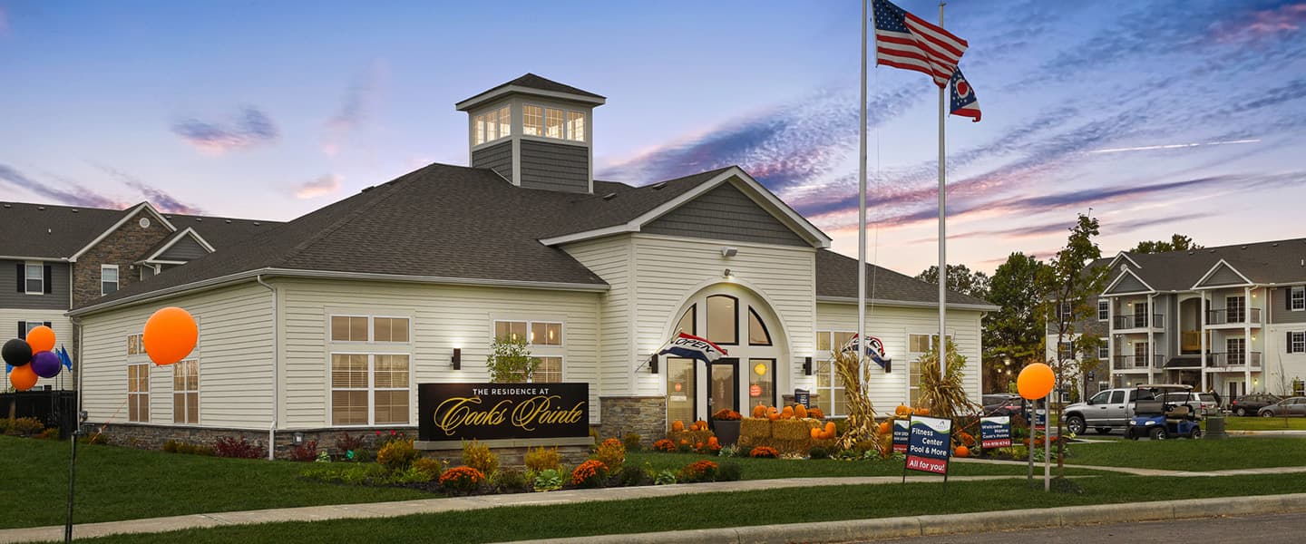 A front-view of an apartment building with inviting landscaping details including trees and bushes.