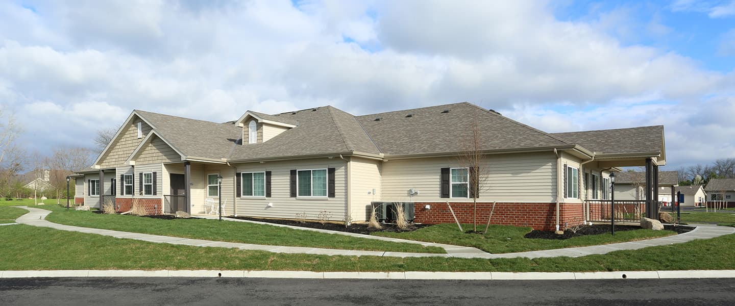 A front-view of an apartment building with inviting landscaping details including trees and bushes.