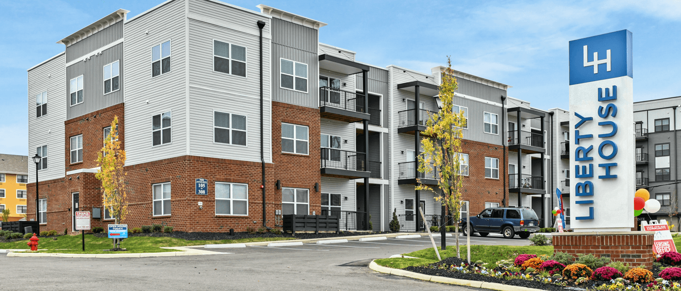 A front-view of an apartment building with inviting landscaping details including trees and bushes.