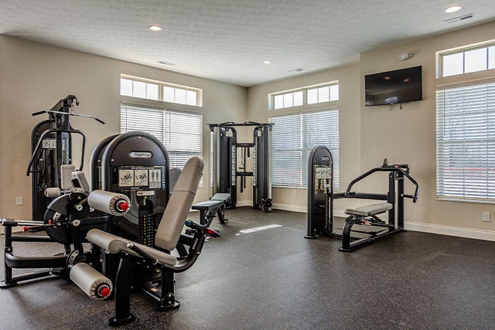 Exercise machines in an apartment gym with a TV on the wall